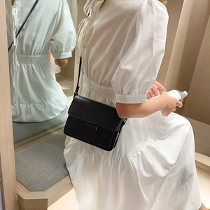 Minimalist black rectangular crossbody flap bag worn by a model in a white dress