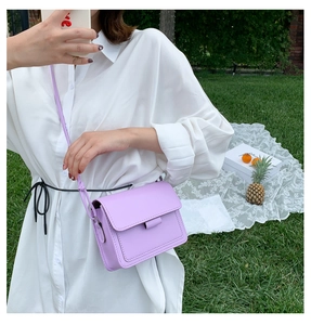 Detail showing lavender square crossbody bag with flap and strap in an outdoor setting