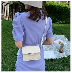 Detail of cream flap crossbody bag with chunky white chain strap on outdoor lawn background