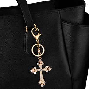 Funkelnder goldener Kreuz-Schlüsselanhänger mit Strasssteinen an einer schwarzen Tasche