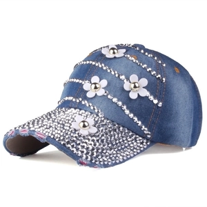 Close-up of white 3D flowers and sparkling rhinestones on washed blue denim baseball cap