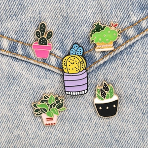 Detail of five cute cactus enamel pins and succulent badges on light blue denim fabric