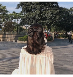 Detailed back view of a large black satin bow hair clip on model in a sunny park