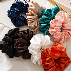 Detailed view of eight satin scrunchies in diverse elegant colors with a smooth silk texture