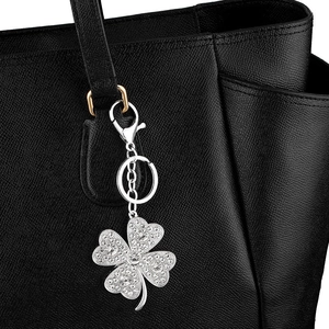 Silver four-leaf clover keychain with sparkling rhinestones on a black leather bag