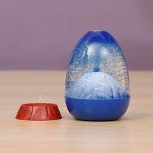 Close-up of blue egg-shaped volcanic sand glass toy with white dynamic liquid and red base