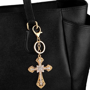 Gold hollowed cross keychain with white rhinestones on a black leather handbag