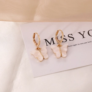 Elegant white butterfly drop earrings with golden hoops on silky champagne fabric