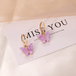 Detailed view of purple butterfly earrings with elegant gold hoops on silk background