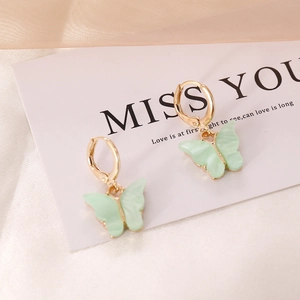 Macro detail of mint green resin butterfly earrings with gold hoops on a display card