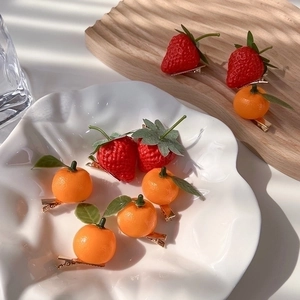 Realistic strawberry and orange hair clips in a ceramic bowl with natural sunlight