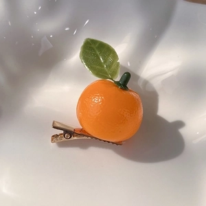 Close-up of realistic orange fruit hair clip with textured peel and green leaf detail