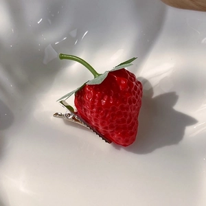 Detailed view of 3D strawberry hair clip with realistic seeds and green leaves on white dish