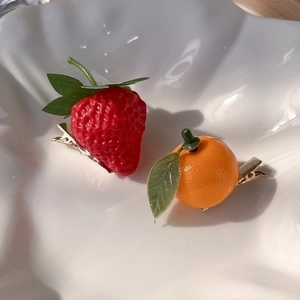 Close-up of strawberry and orange hair clips in a white ceramic dish