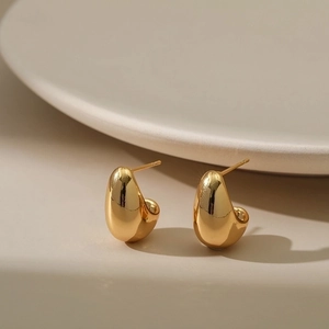 Minimalist 18K gold bean drop earrings with high-polish metallic finish on a beige surface