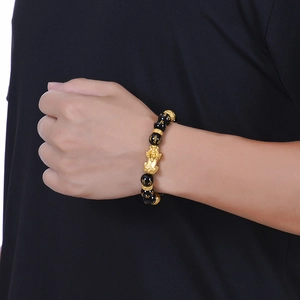 Detail of black agate beads with golden mantras and a PiXiu charm on a model wrist