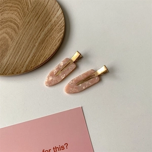 Macro detail of two pink marble-textured acetate hair clips with gold metal base