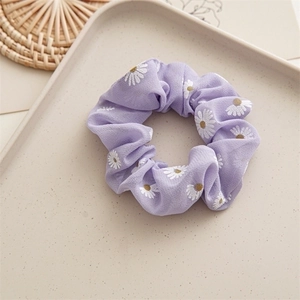 Close-up of purple chiffon scrunchie with white daisy floral print on beige tray