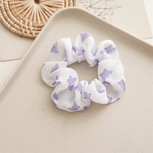 Close-up of white chiffon hair scrunchie with purple butterfly pattern on beige tray