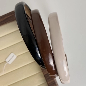 Three minimalist glossy headbands in black, brown, and beige on a jewelry display tray