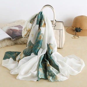 Elegant silk scarf with green floral patterns draped on a handbag with sun hat