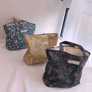 Trois sacs en coton à fleurs bleu, beige et vert posés sur une literie blanche