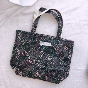Détail d'un petit sac en tissu floral avec sangle en coton blanc et étiquette tissée