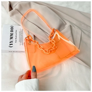 Detail of orange transparent PVC baguette bag with thick matching chain on white fabric