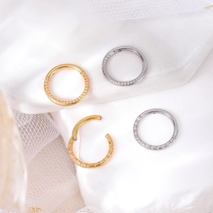 Close-up of gold and silver heart-engraved nose rings on soft white lace background