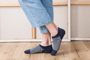 Detailed view of dark blue and white striped low-cut socks worn on feet with wooden background