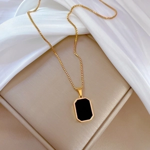 Elegant gold box chain necklace with a geometric black rectangular pendant on white silk
