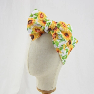 Detail of baby headband featuring large sunflower print bow on a textured white fabric