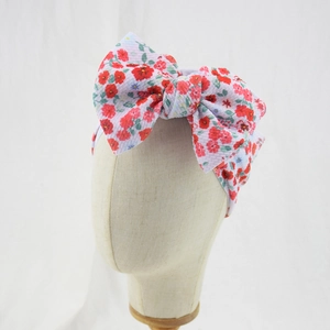 Detail of white infant headband with a large red floral print bow on a beige head form
