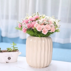 Pink and white artificial carnations in a beige ceramic vase on a marble table