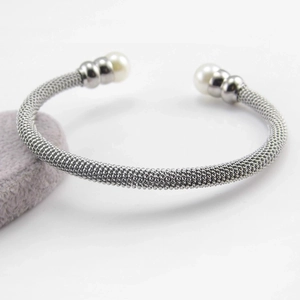 Detail of silver mesh cuff bracelet with white faux pearls on a gray velvet stand