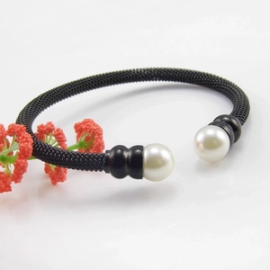 Detail of rose gold bangle with black mesh weave and dual white pearl accents