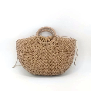Detail of moon-shaped straw handbag featuring round handles and drawstring fabric lining