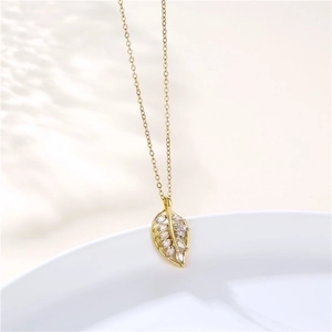 Close-up of golden leaf pendant with sparkling zircons on a white ceramic plate