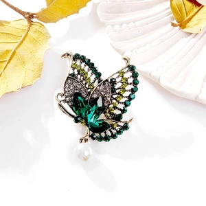 Detailed close-up of a butterfly brooch with sparkling green rhinestones and a pearl drop