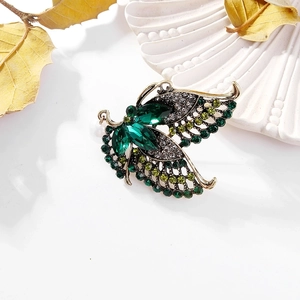 Detailed close-up of a vintage golden peacock brooch with green rhinestones and pearl