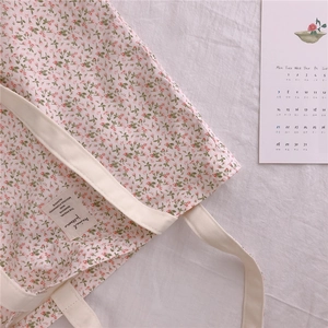 Close-up of floral cotton tote bag with cream straps and decorative label on soft background