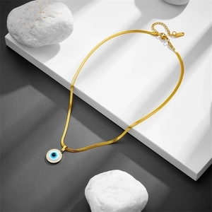 Gold evil eye pendant necklace with snake chain on modern geometric display stand