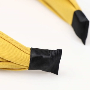 Solid yellow fabric knotted headband featuring black capped ends on a white background