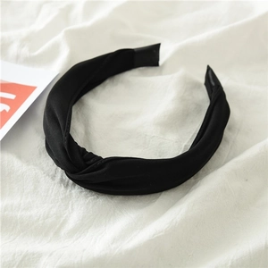 Detailed view of black knotted fabric headband on a soft white linen background