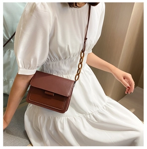 Detail view of a vintage dark brown leather crossbody bag with amber chain on white dress