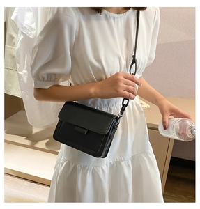 Detail of a minimalist black leather crossbody bag with chain strap and flap closure