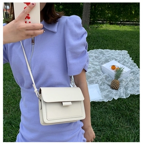 Detail of a beige faux leather flap crossbody bag with decorative stitching on grass