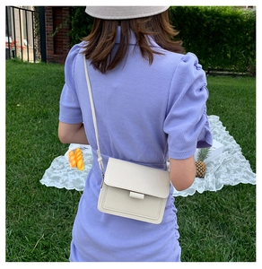 Detail of cream crossbody bag showing clean stitching and elegant clasp in nature setting