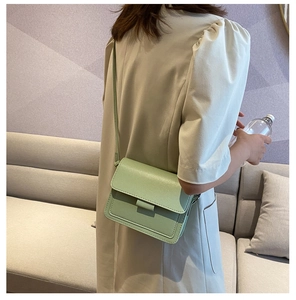 Rear view of a minimalist light green leather crossbody bag worn by a model in a cafe
