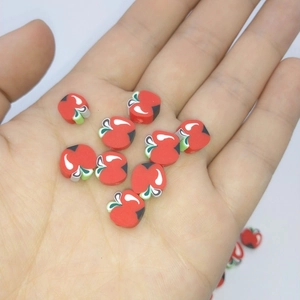 Detail shot showing small red apple-shaped polymer clay beads held in palm for scale
